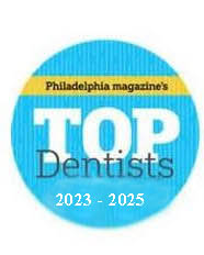 The image features a circular logo with text that reads  PHILADELPHIA MAGAZINE S TOP DENTISTS  in white letters on a blue background, accompanied by a small graphic of a top hat.
