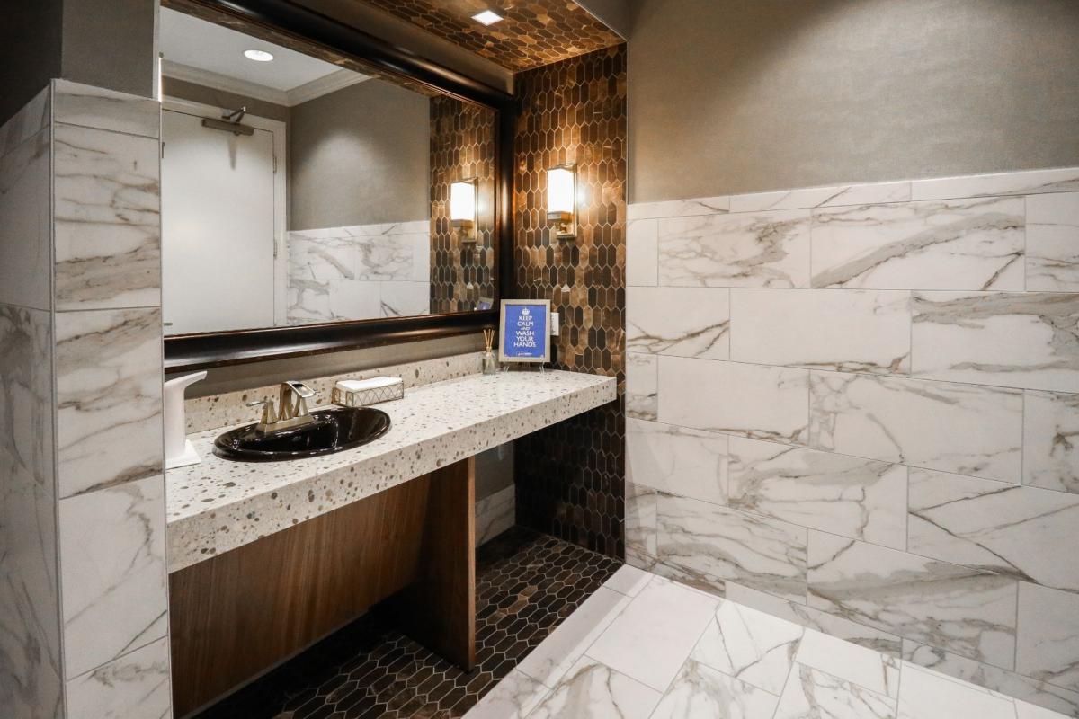 The image shows a bathroom with marble walls, a sink, and a mirror, featuring a modern design with a sleek aesthetic.