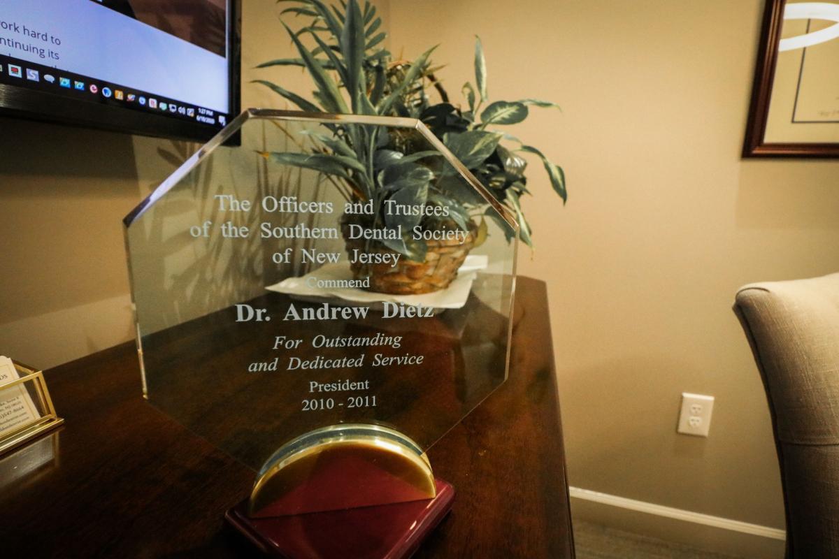 The image displays a formal plaque on a desk with text indicating recognition for an individual's service, placed against a blurred background of an office setting.