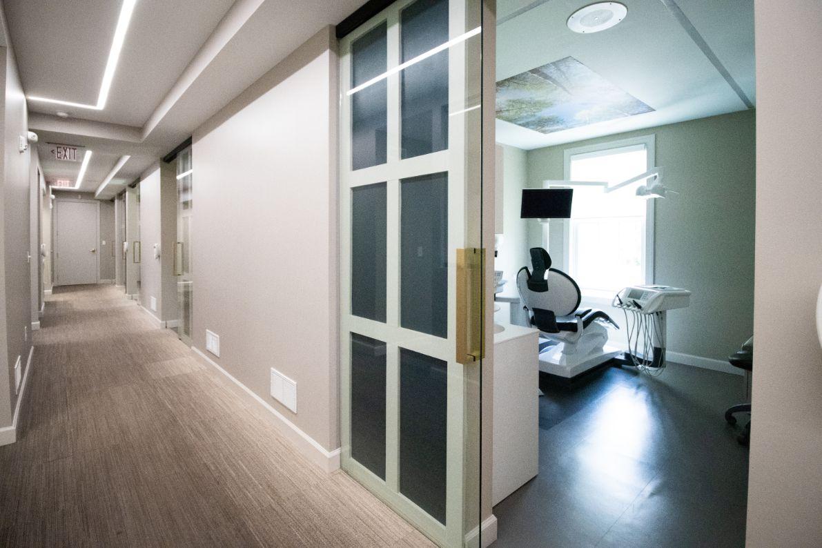 The image shows a hallway with two open doors leading into separate rooms, one of which contains medical equipment.