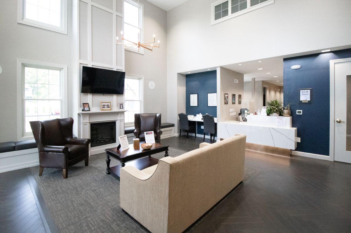 The image depicts an interior view of a well-lit waiting room with blue walls, white trim, a fireplace, seating area, television, and a reception desk.