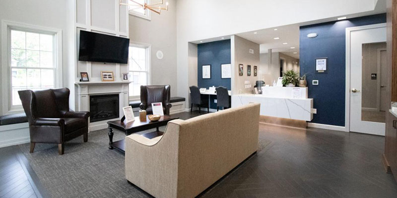 The image depicts a modern office reception area with a sleek, contemporary design featuring a wooden desk and a white countertop.