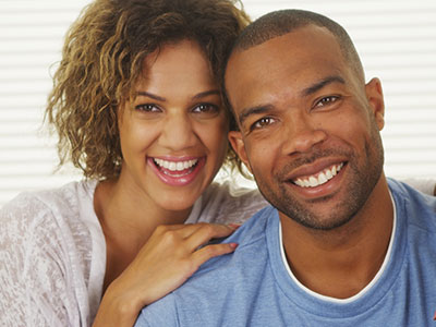 A man and woman smiling at the camera, with the man wearing a blue t-shirt and the woman in a white top.