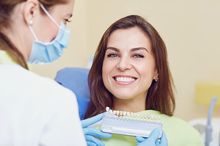A woman is smiling at the camera while receiving dental care from a professional who is holding a dental tool.