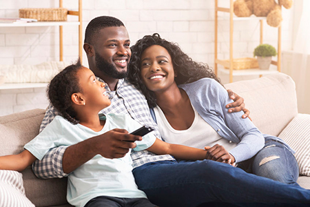 A family enjoying time together on a couch, with a man holding a child and another adult sitting beside them.