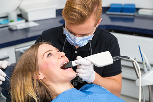 A dental hygienist using an electric toothbrush on a patient s teeth while sitting in a dentist chair.