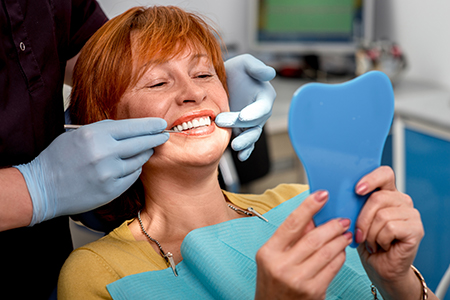 In the image, there s a woman seated with a dental professional who is showing her a plastic model of her teeth.