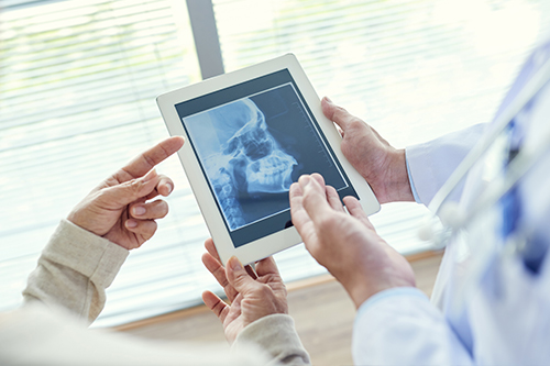 The image shows two individuals interacting with a tablet displaying an X-ray image, with a medical professional holding the device and another person viewing it.