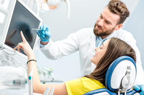 A dental professional is explaining something on a computer screen to a patient with a headset and remote control in a modern dental office setting.