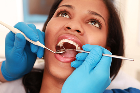 A woman receiving dental care with her mouth open while sitting in a dental chair, surrounded by dental tools and equipment.