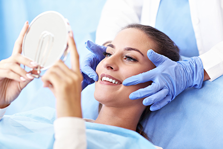 A woman receiving facial treatment in a medical setting with a professional holding up a magnifying glass.